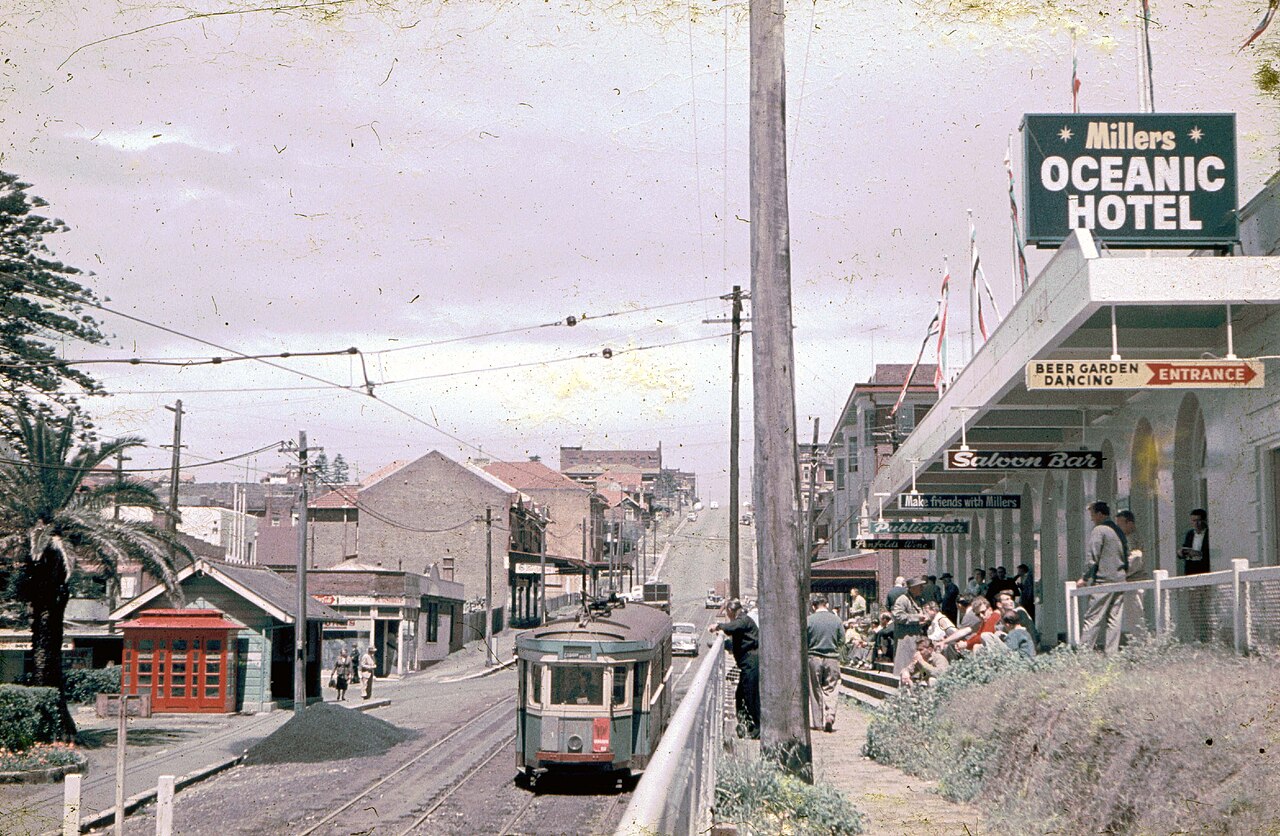 A tram climbs a street past the Oceanic Hotel sign, Coogee, Sydney, 1960