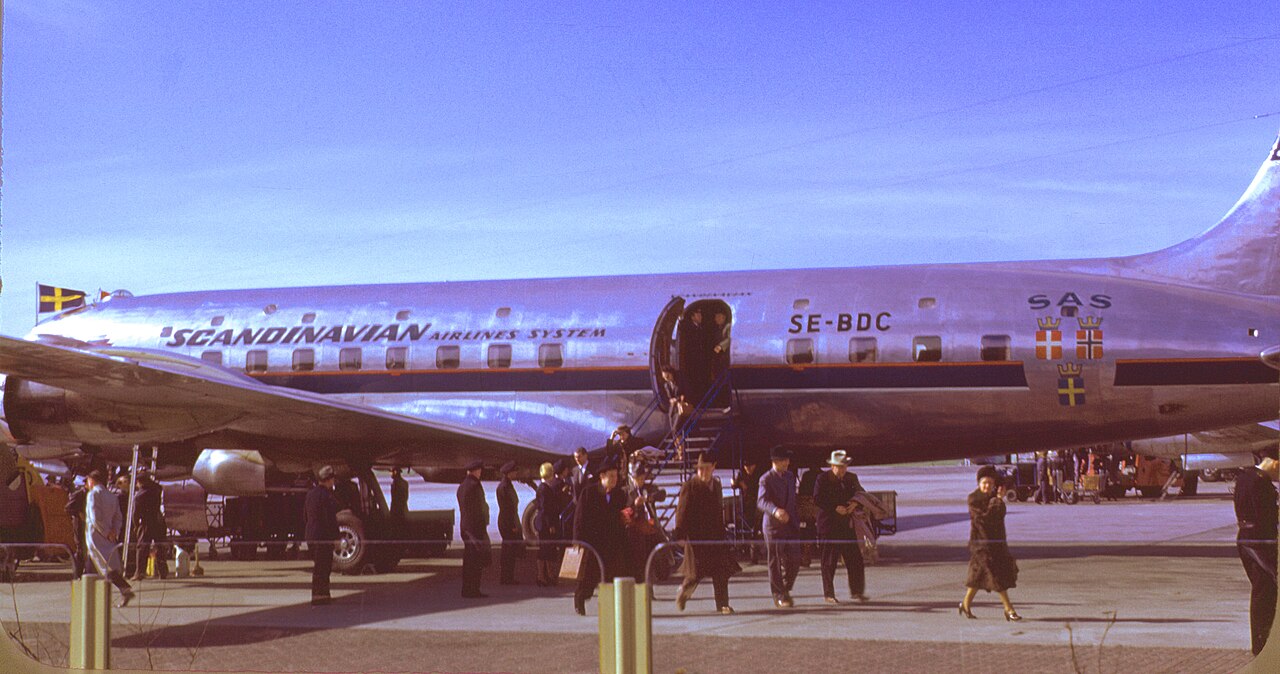 Passengers cross the apron to board a silver SAS Douglas DC-6