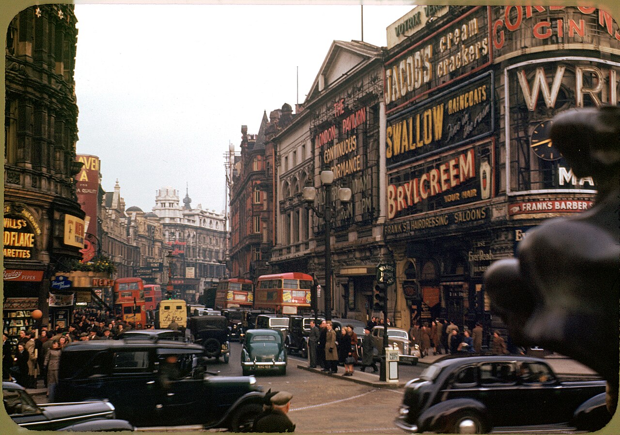Piccadilly Circus with painted advertising signs, black cars and a red double-decker bus, London, about 1949